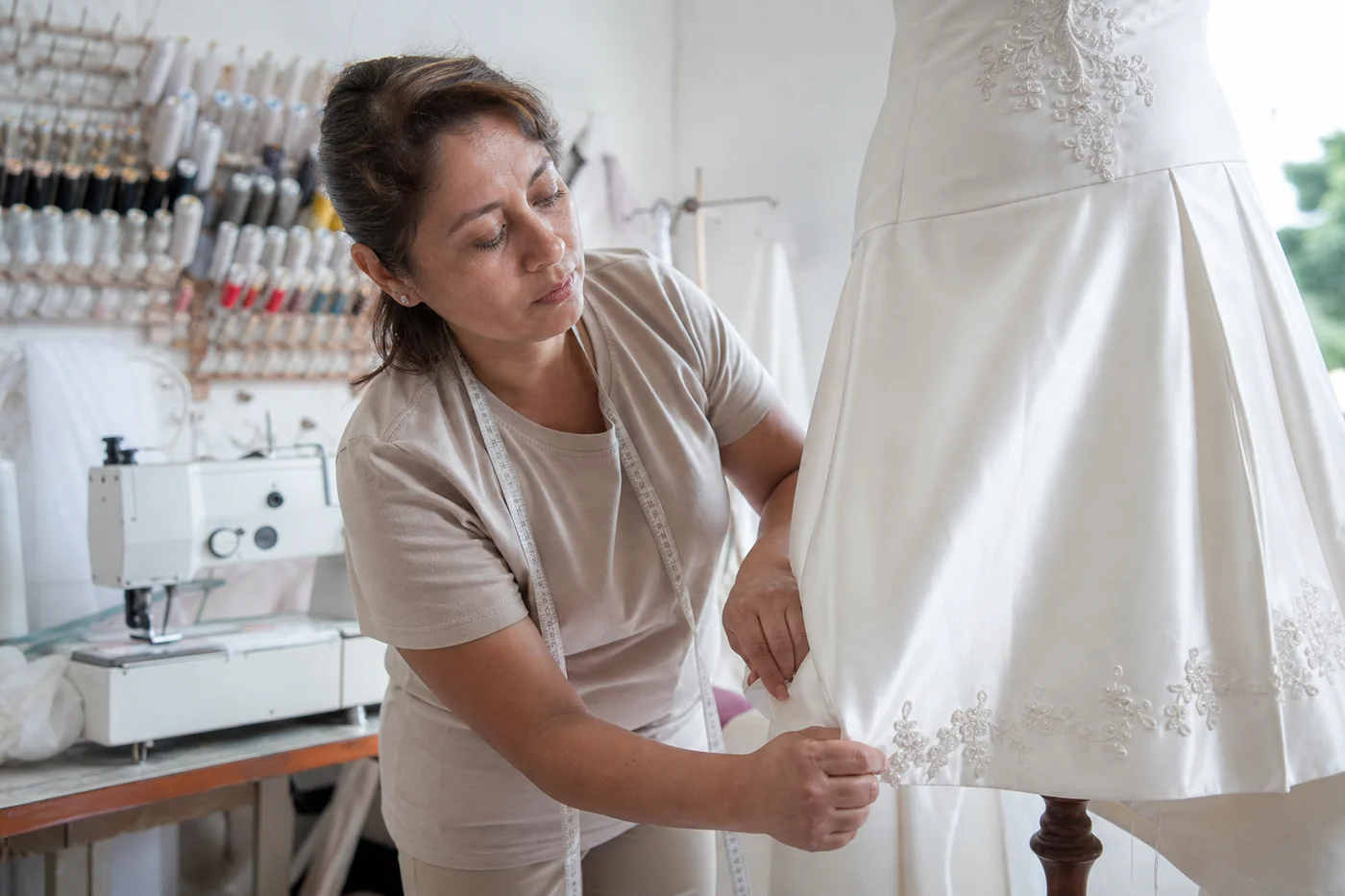 Costurera ajustando el dobladillo de un vestido de novia en el taller con alfileres