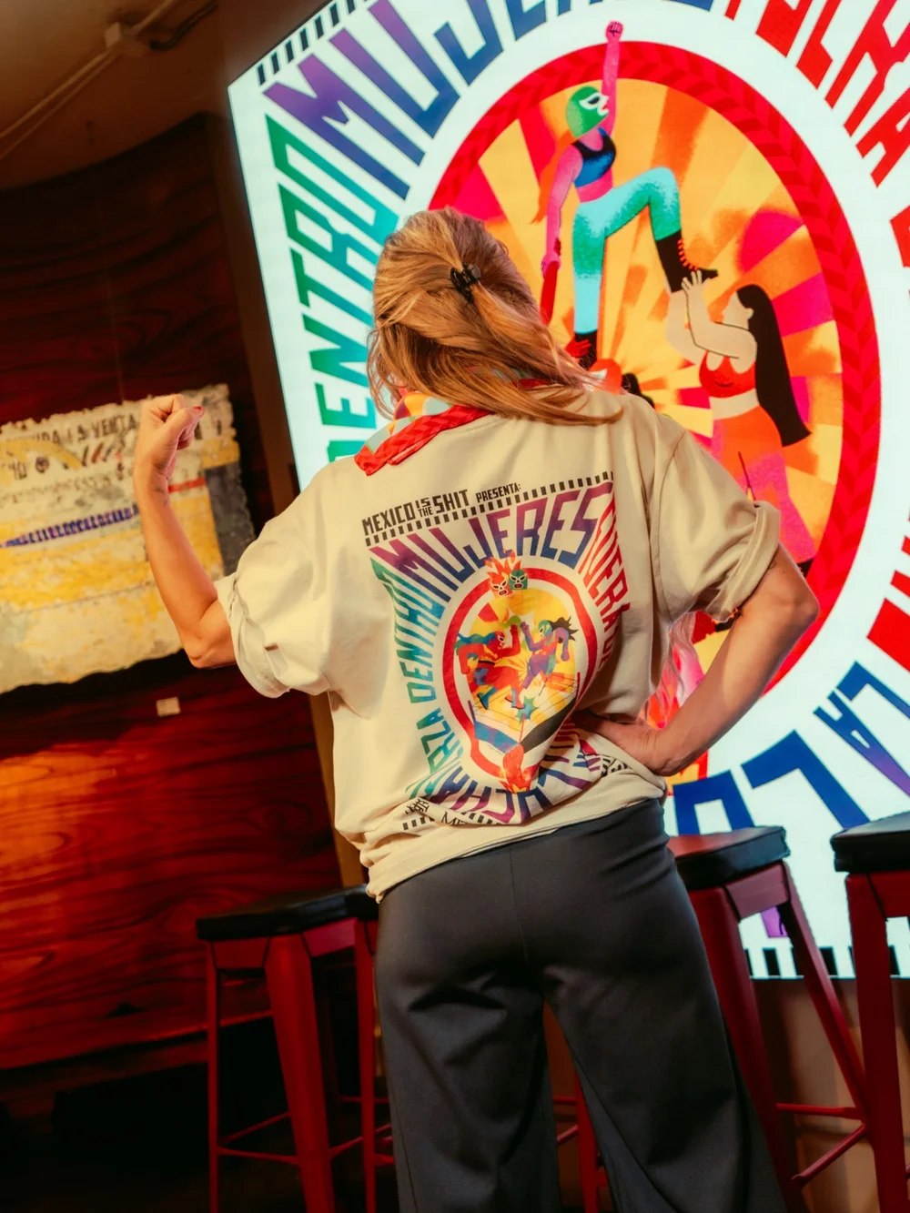 Mujer con la playera «Mujeres en la lucha» de MITS frente a la pantalla de la colección