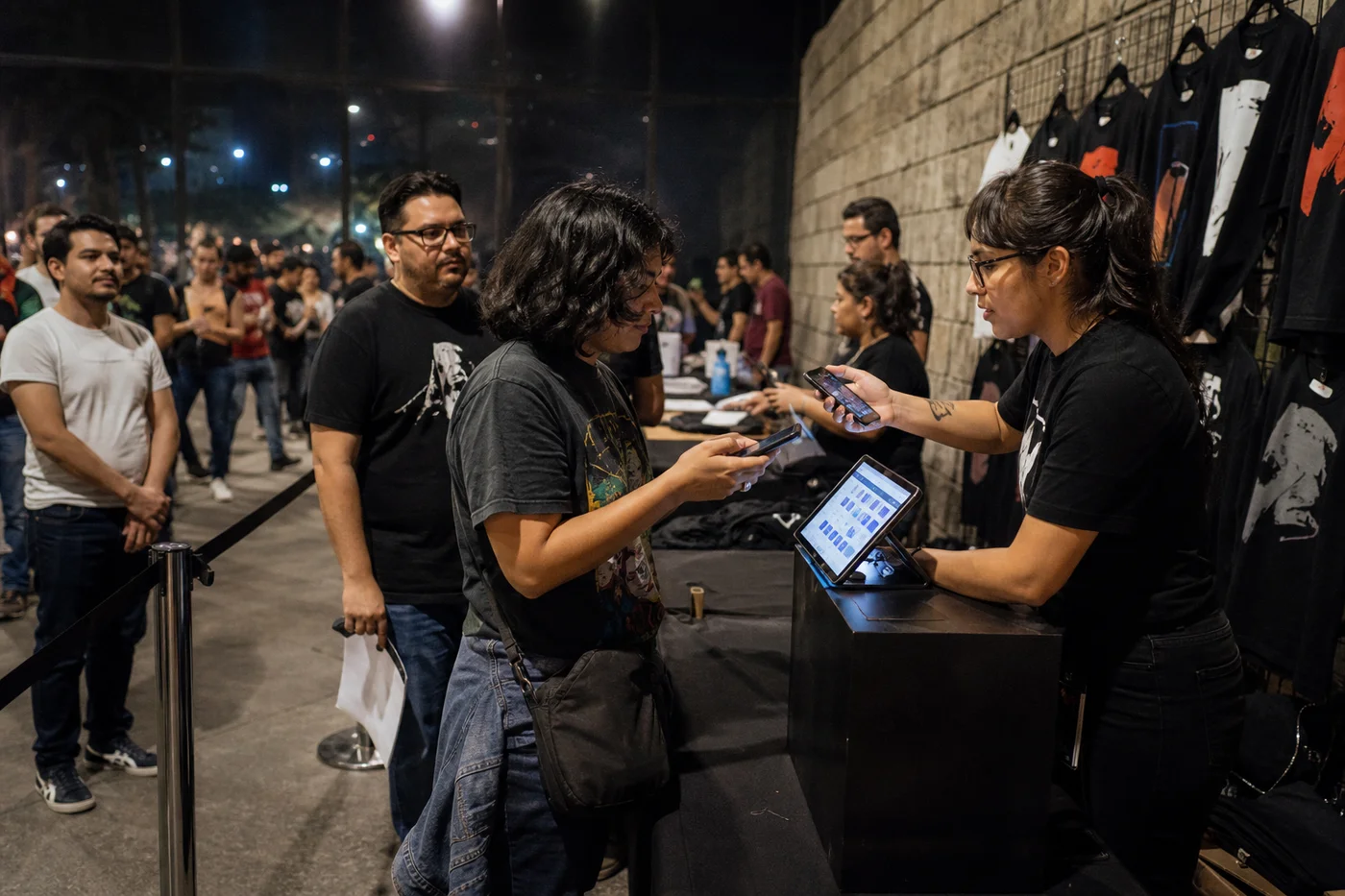 Fila ordenada de asistentes frente al módulo de merch con staff escaneando celulares