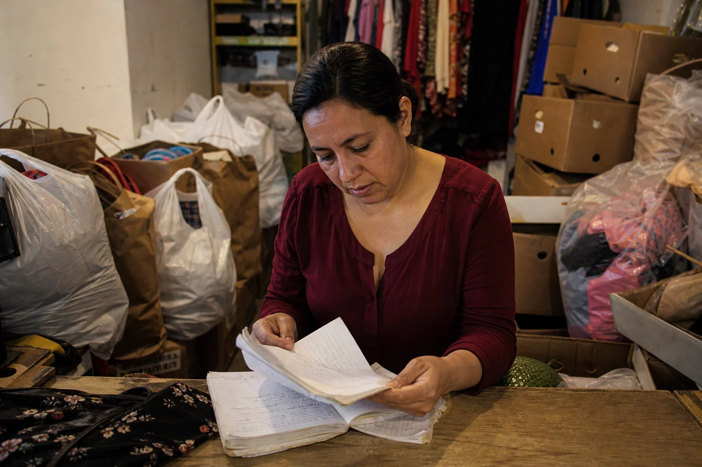 Dueña de una tienda de consignación entre bolsas y cajas de piezas recibidas, hojeando una libreta