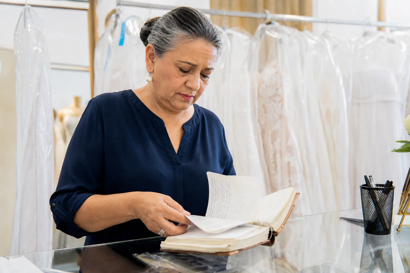 Dueña de una casa de novias hojeando un cuaderno de citas y abonos entre vestidos enfundados